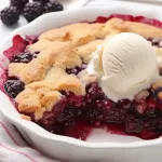 Close-up of a serving of Blackberry Cobbler showing the fluffy interior and berries, paired with a cup of coffee.