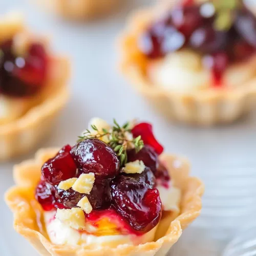 Close-up of a bite-sized appetizer featuring melted brie, tangy cranberry topping, and a crisp shell.