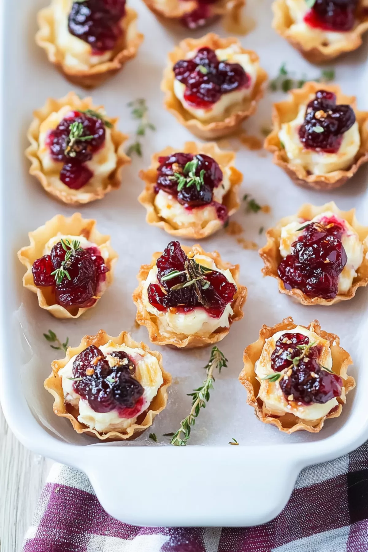 A tray of golden cranberry brie bites, garnished with herbs, ready to serve for a festive gathering.