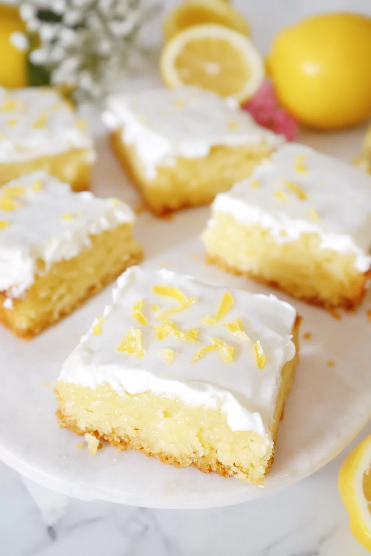 A serving platter with neatly cut squares topped with a vibrant lemon drizzle