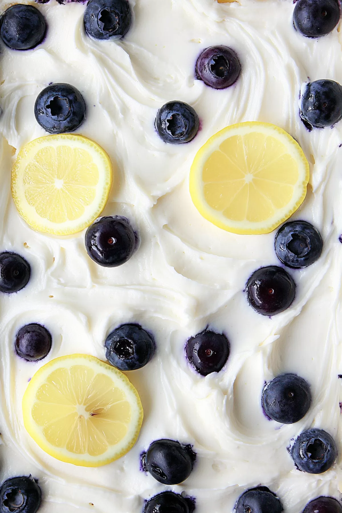 Close-up of a moist cake topped with vibrant blueberries and smooth lemon icing.