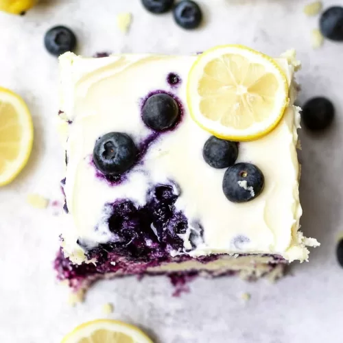 Overhead view of a frosted sheet cake decorated with fresh blueberries and lemon slices.