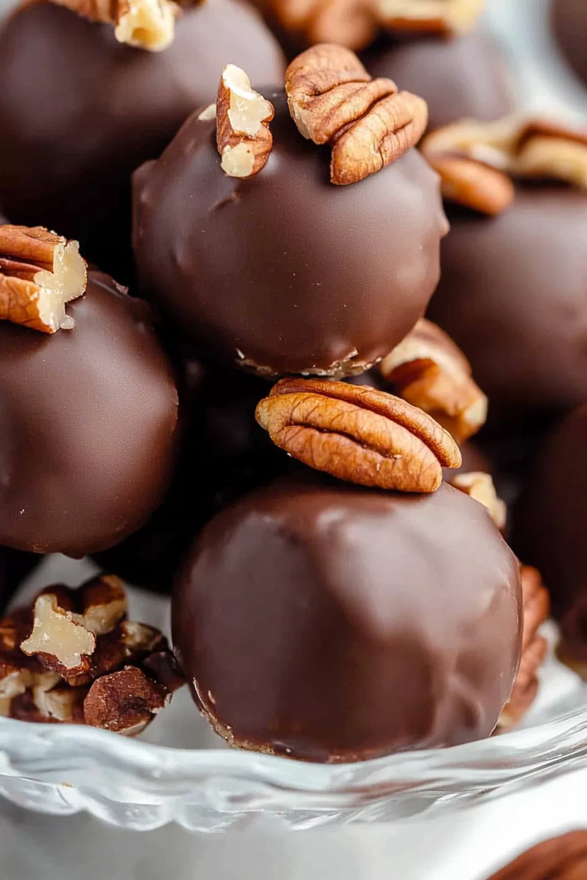 Close-up of chocolate-coated truffles with pecan toppings on a glass pedestal.