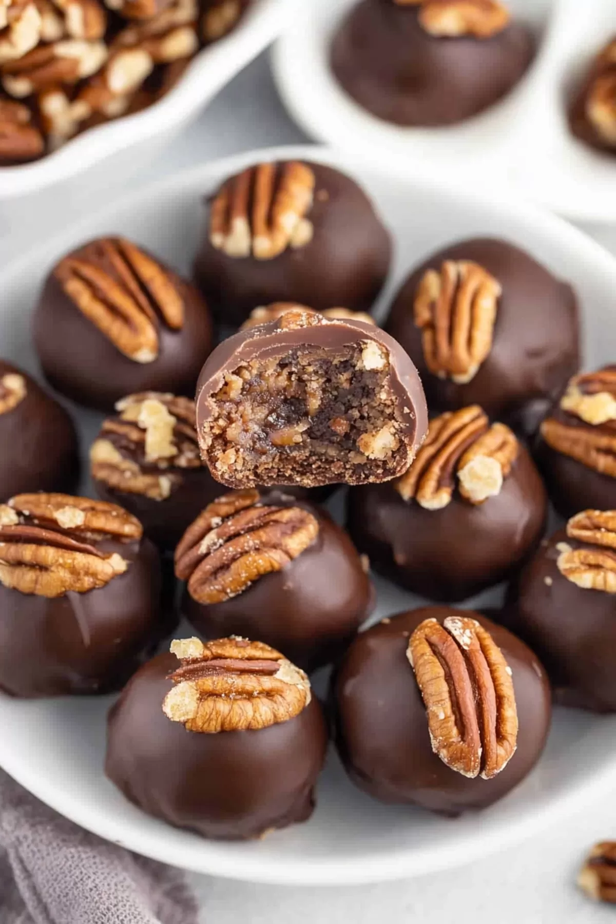 A plate of bite-sized pecan treats with glossy chocolate shells and crunchy nut accents.