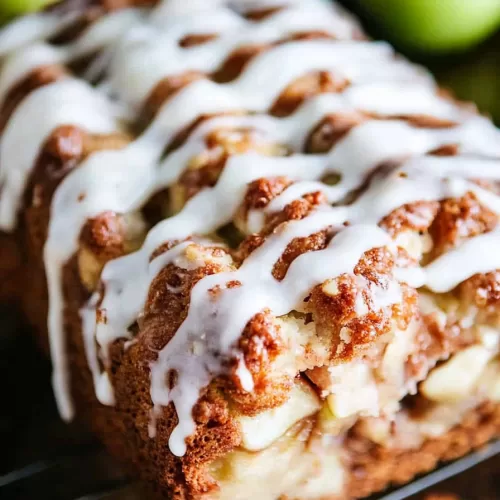 Glazed apple fritter bread cooling on a rack, surrounded by fresh green apples in the background.