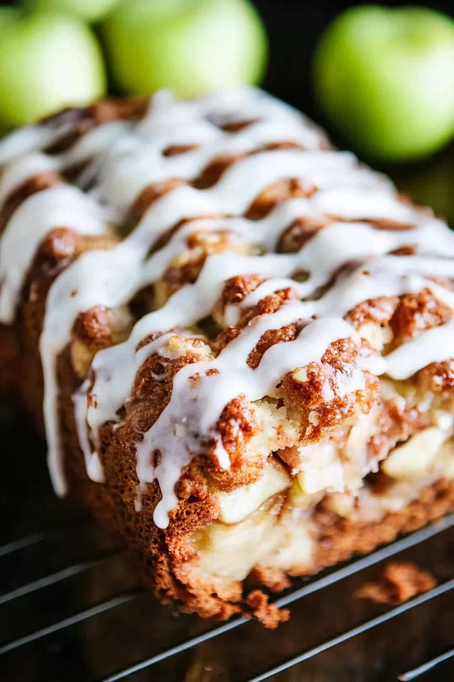 Glazed apple fritter bread cooling on a rack, surrounded by fresh green apples in the background.