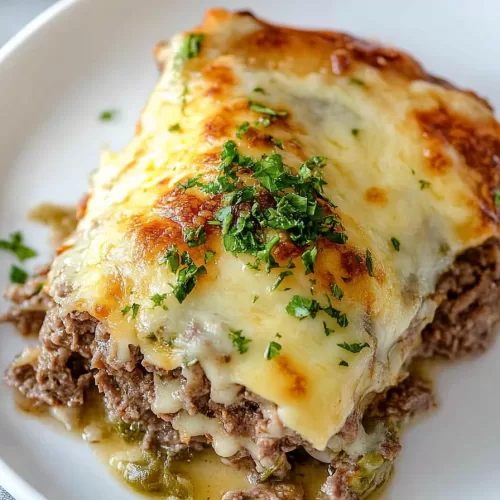 A comforting dish of baked Philly cheesesteak with gooey cheese, diced green peppers, and a rich sauce.