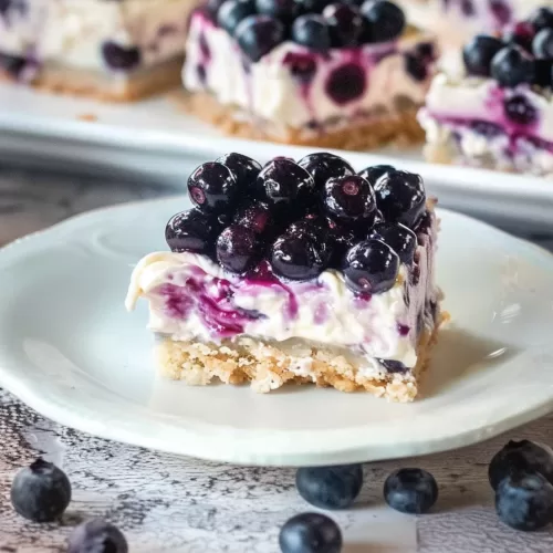 A creamy blueberry dessert square with fresh berries on a crumbly crust, served on a white plate.