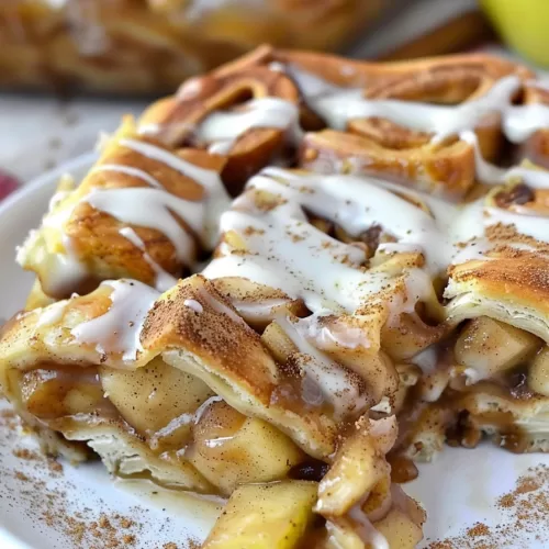 A slice of layered caramel apple cinnamon roll lasagna served on a white plate, topped with creamy icing.