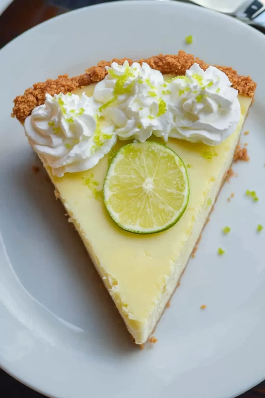 Close-up of a creamy key lime pie with a graham cracker crust, topped with fresh whipped cream and lime zest.