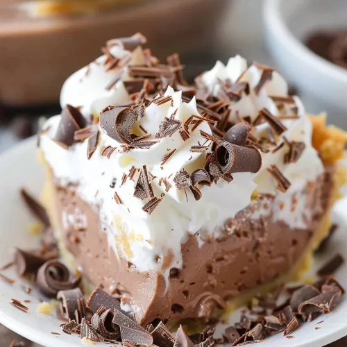 A close-up of a decadent slice of chocolate pudding pie topped with whipped cream and chocolate shavings.