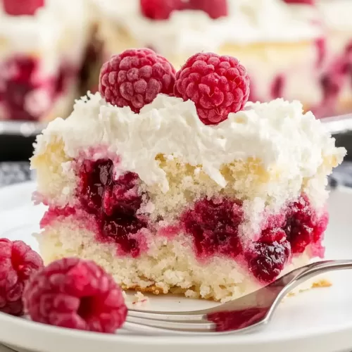 A single slice of raspberry poke cake on a plate, showcasing the rich layers of raspberry and coconut.