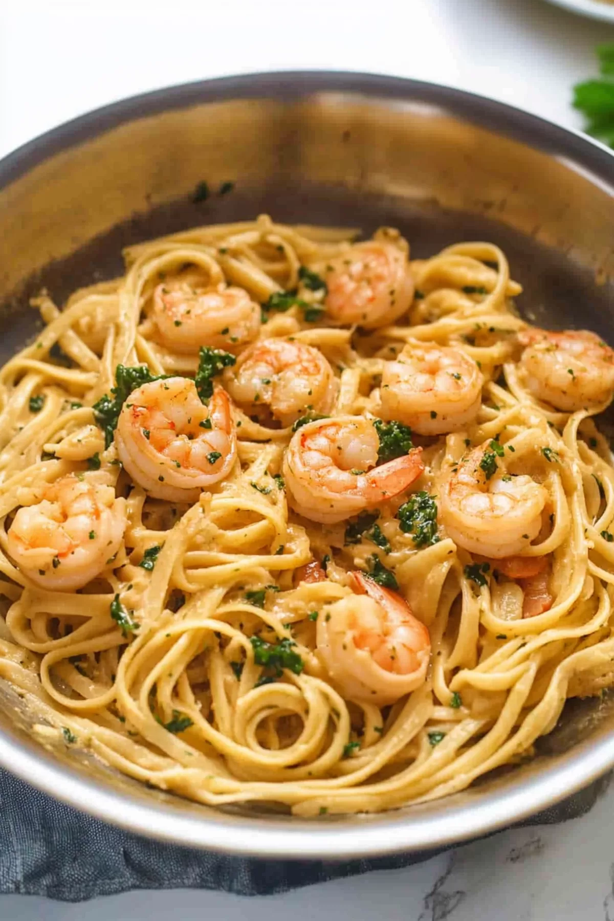 A bowl of pasta in creamy garlic sauce with plump shrimp and a sprinkle of parsley.