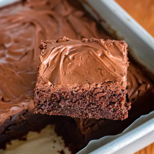 Close-up of a single brownie square being lifted from a pan, showing its rich, moist texture.