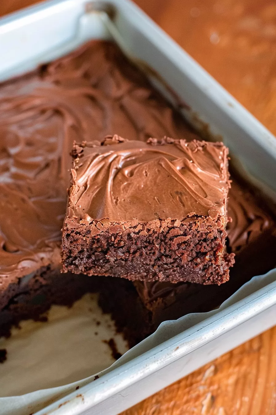 Close-up of a single brownie square being lifted from a pan, showing its rich, moist texture.