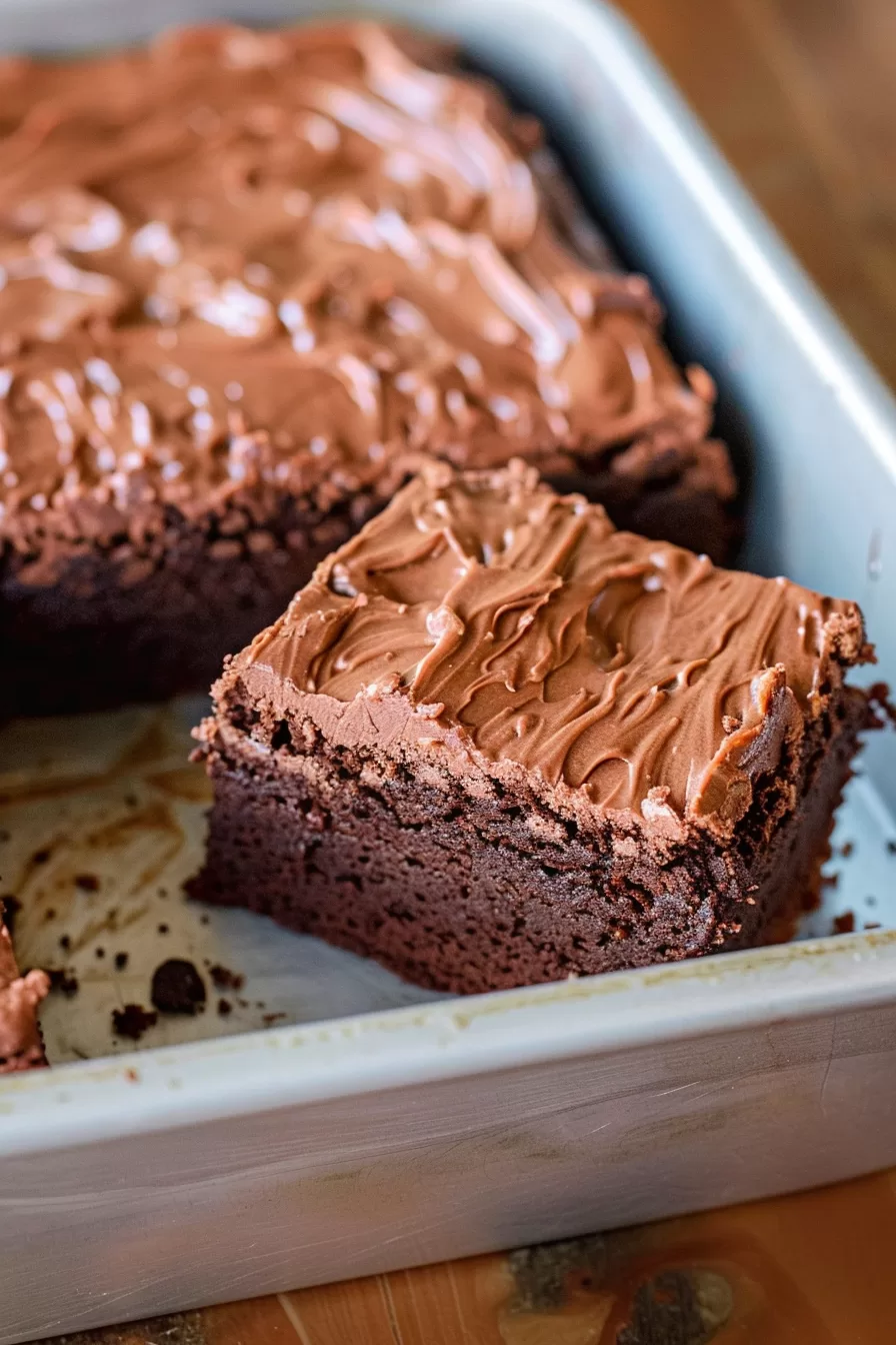 A pan of frosted brownies with one slice missing, revealing the dense and chewy interior.