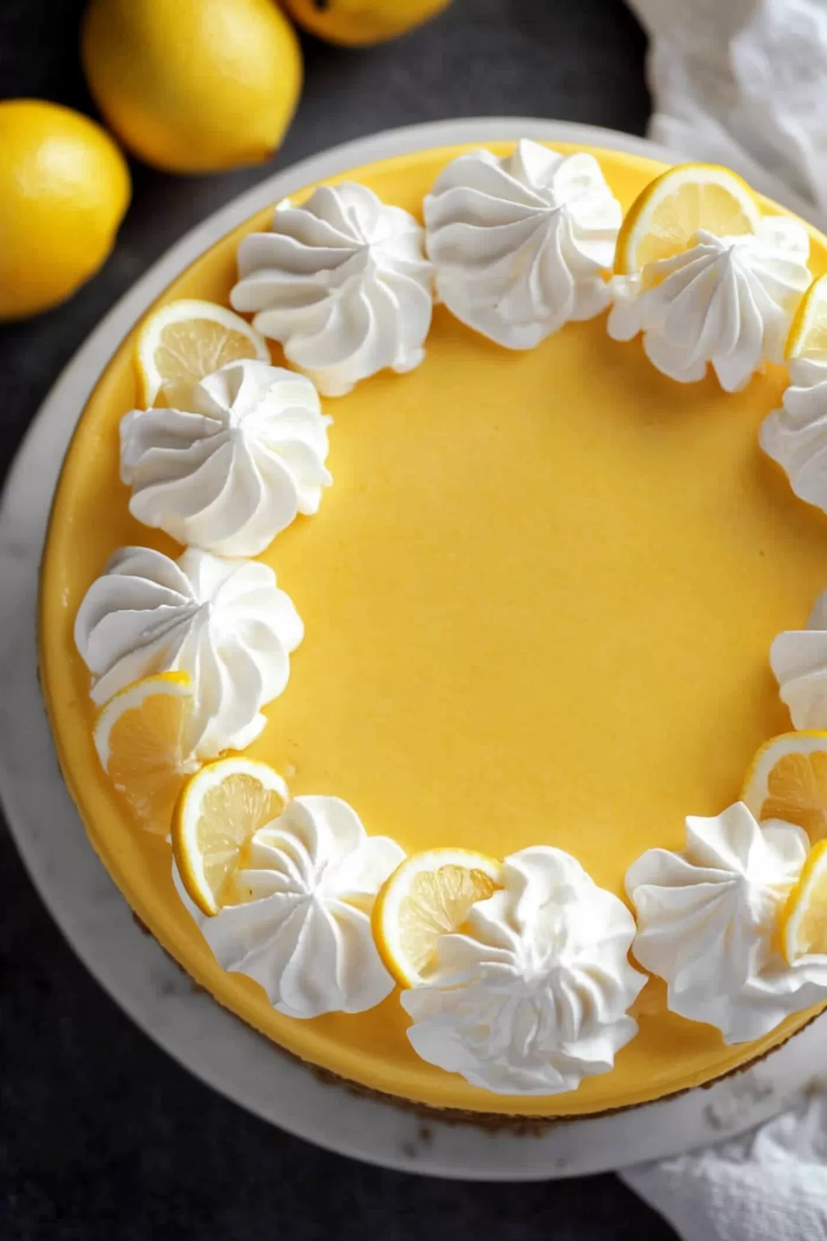 Overhead shot of a whole lemon cheesecake, decorated with piped whipped cream and fresh lemon slices.