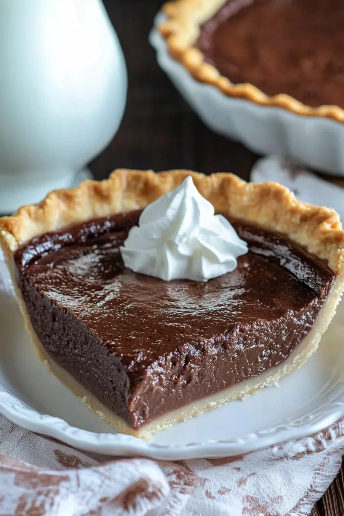 A close-up slice of rich chocolate cream pie topped with a dollop of whipped cream on a white plate.