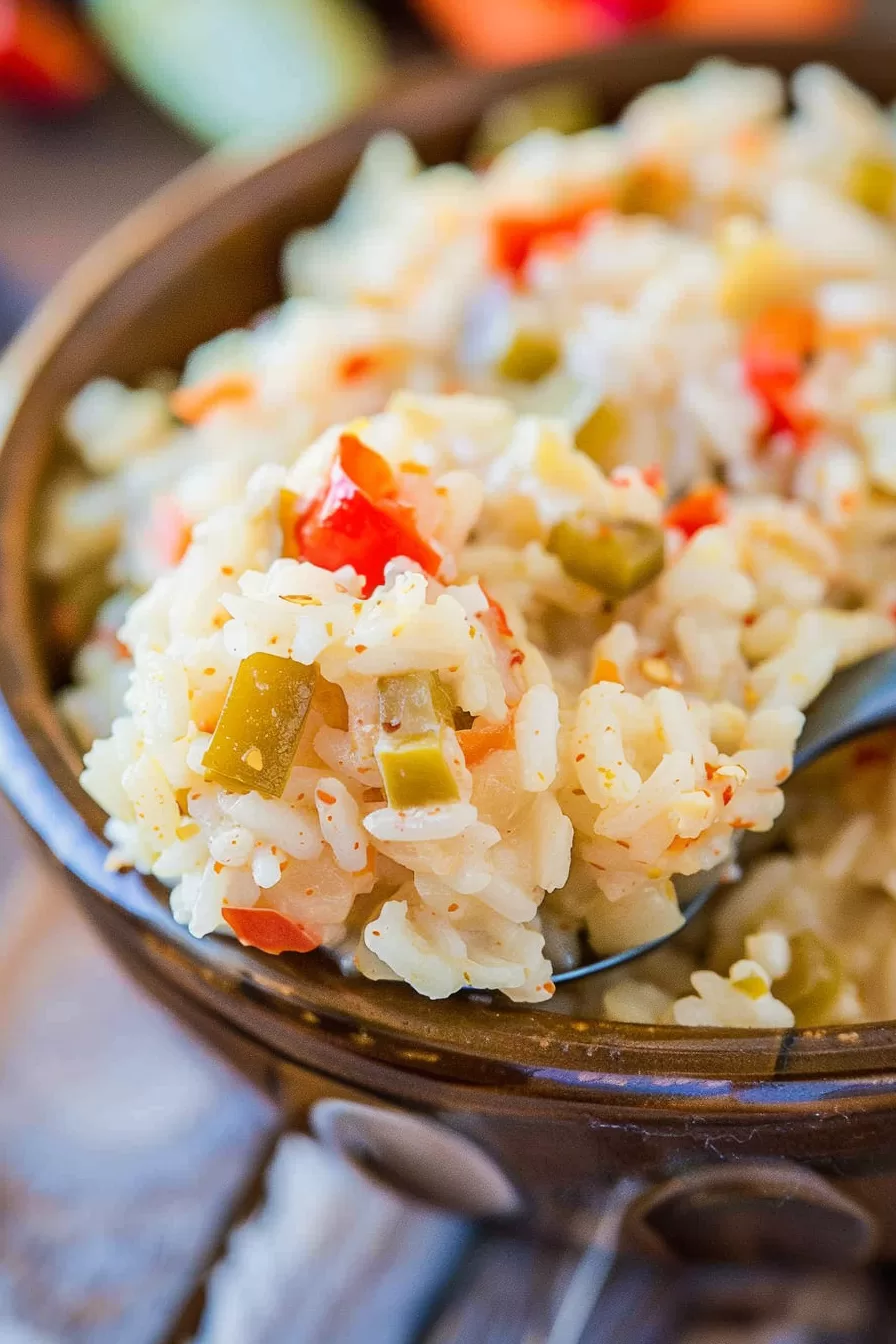 A spoonful of cheesy Pepper Jack rice bake lifted from a baking dish, showcasing its creamy and colorful texture.