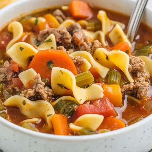 A cozy bowl of soup filled with beef, noodles, and vegetables, served on a rustic table.