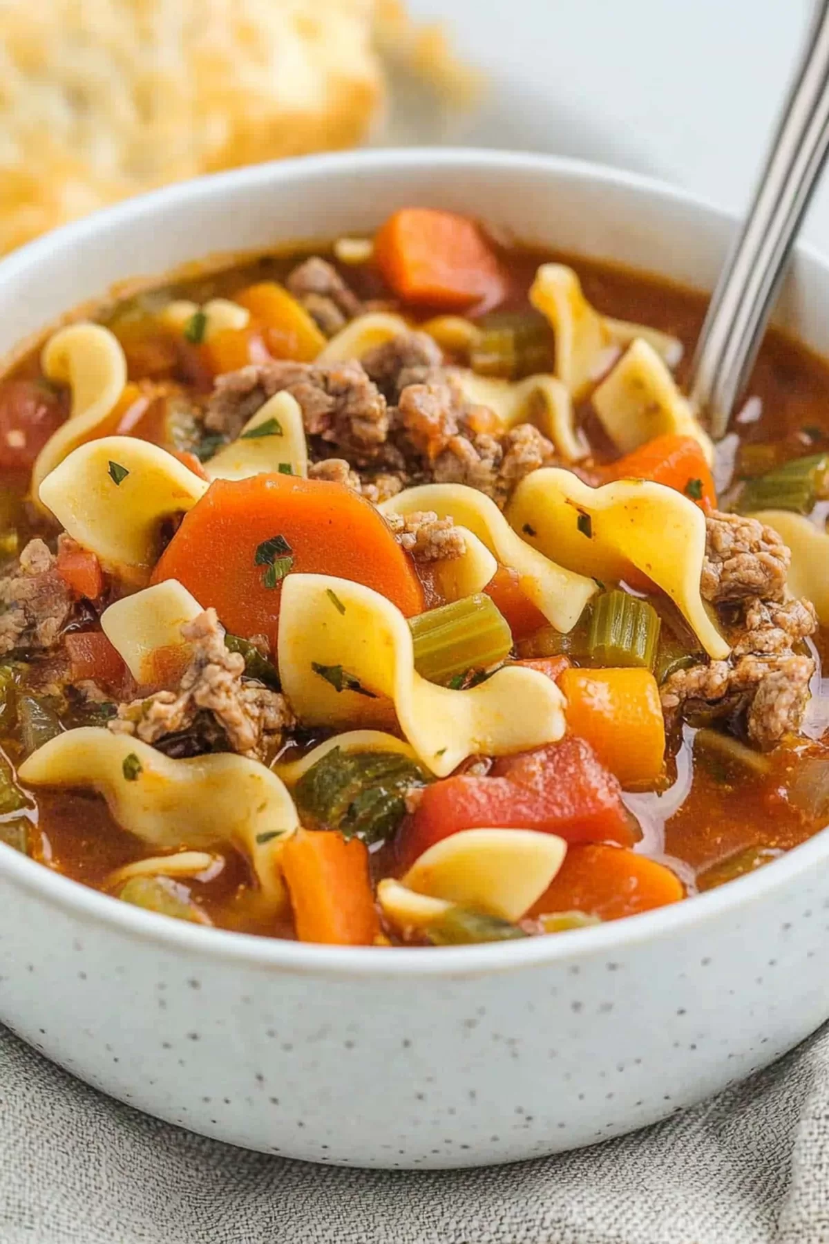 A cozy bowl of soup filled with beef, noodles, and vegetables, served on a rustic table.