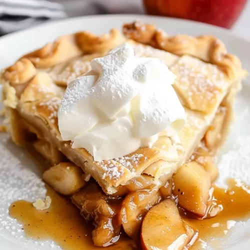 A slice of apple pie topped with whipped cream, revealing tender cinnamon-spiced apple filling and flaky crust.