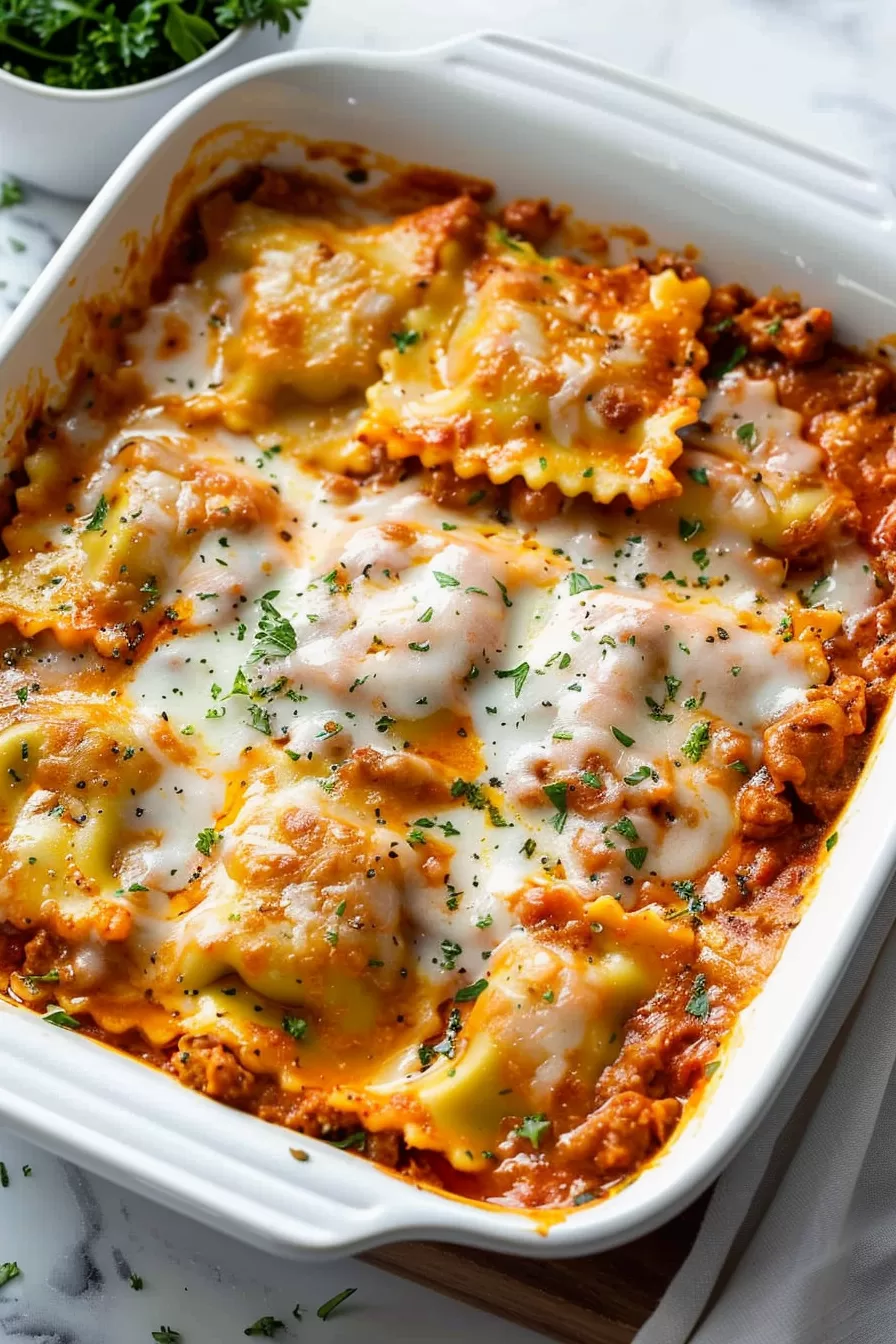 A family-style dish of baked ravioli casserole, featuring bubbly cheese and a rich tomato sauce in a white baking dish.