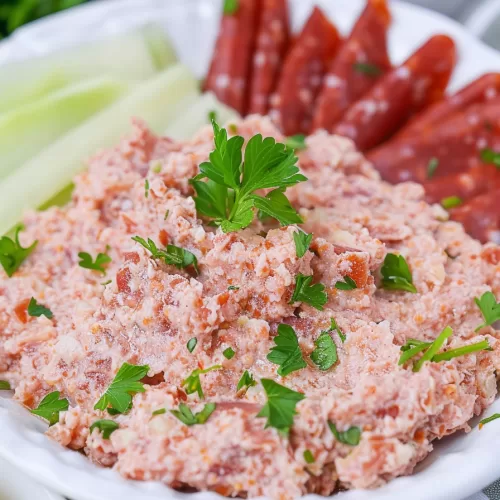 Bologna salad on a charcuterie board with celery sticks, salami slices, and dipping sauce.