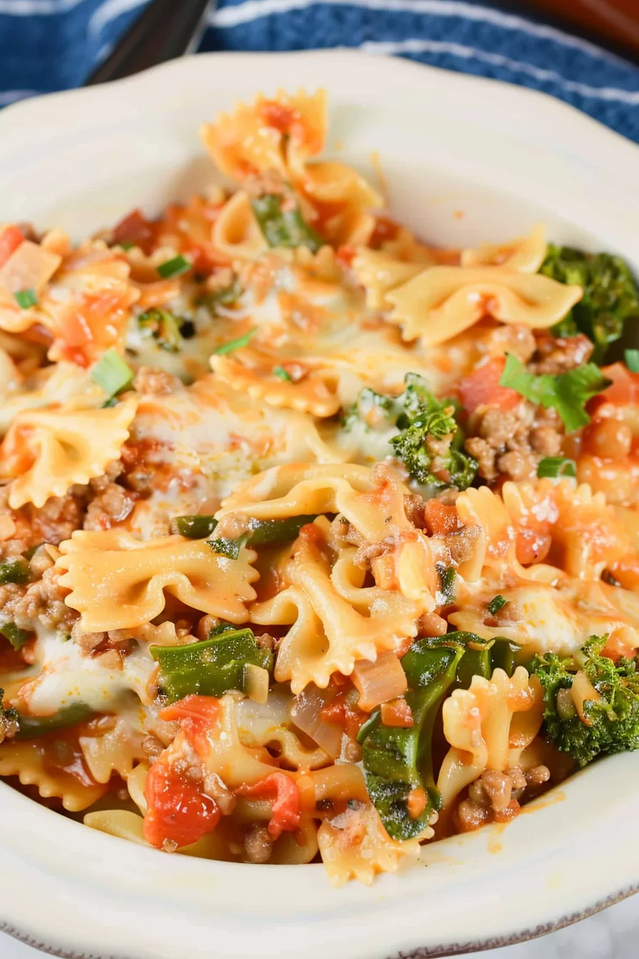 A close-up of bowtie pasta layered with savory sauce, melted cheese, and fresh vegetables, served in a warm casserole dish.