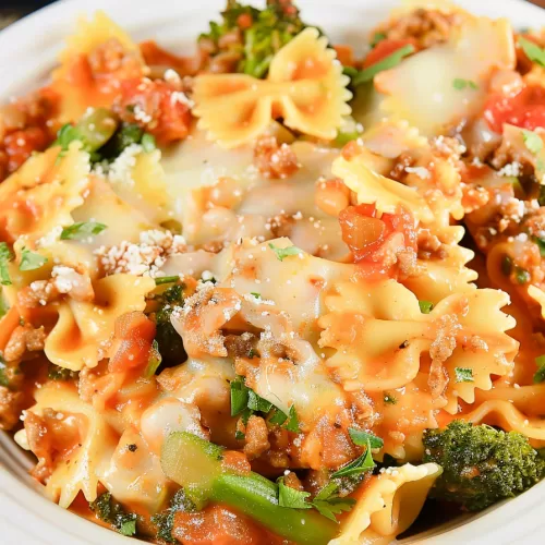 Golden and bubbly bowtie pasta casserole fresh out of the crockpot, topped with melted cheese and vibrant greens.