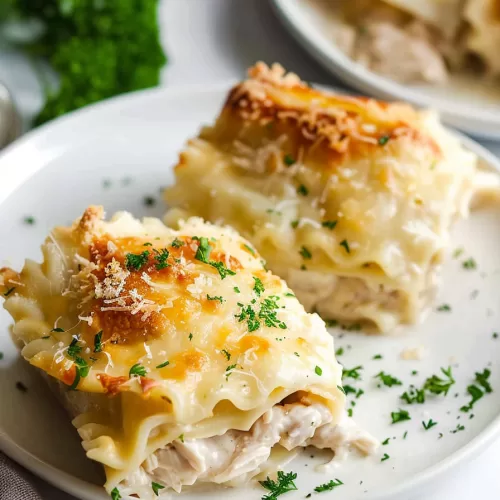 A plate with a single serving of Chicken Alfredo lasagna roll-up, garnished with parsley, showing creamy Alfredo sauce and shredded chicken filling.