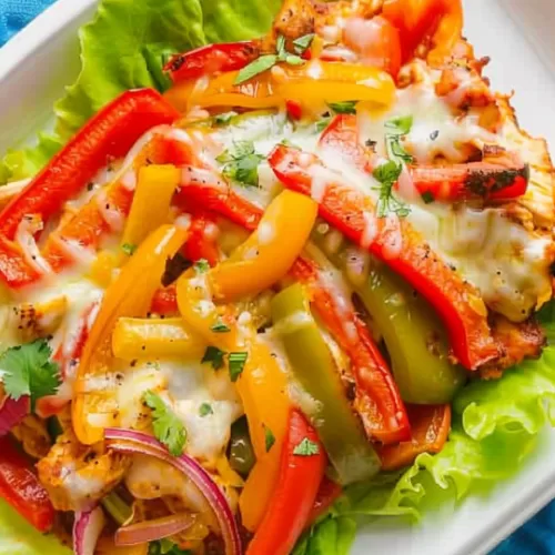 A plate of chicken fajita casserole served on lettuce leaves, topped with red, yellow, and green bell peppers and melted cheese.