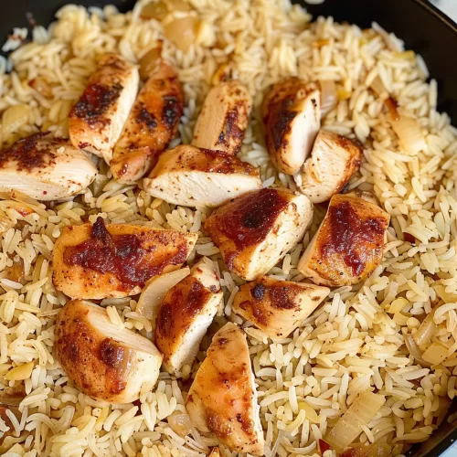 Close-up of a skillet with seared chicken and fluffy parmesan-infused rice, topped with parsley for a vibrant finish.