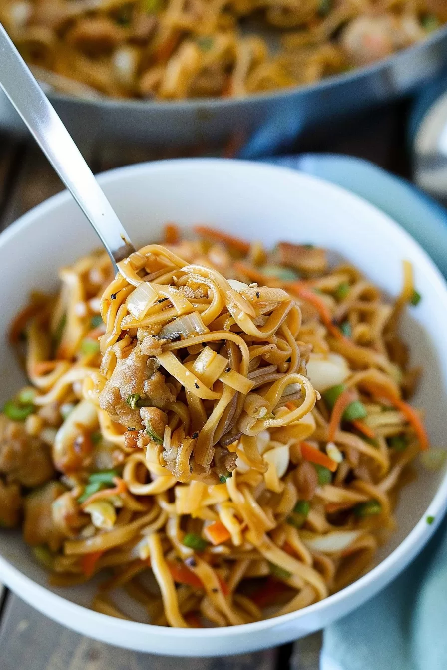 A bowl of noodle stir-fry with chicken, broccoli, and carrots, garnished with fresh herbs, ready to be enjoyed.