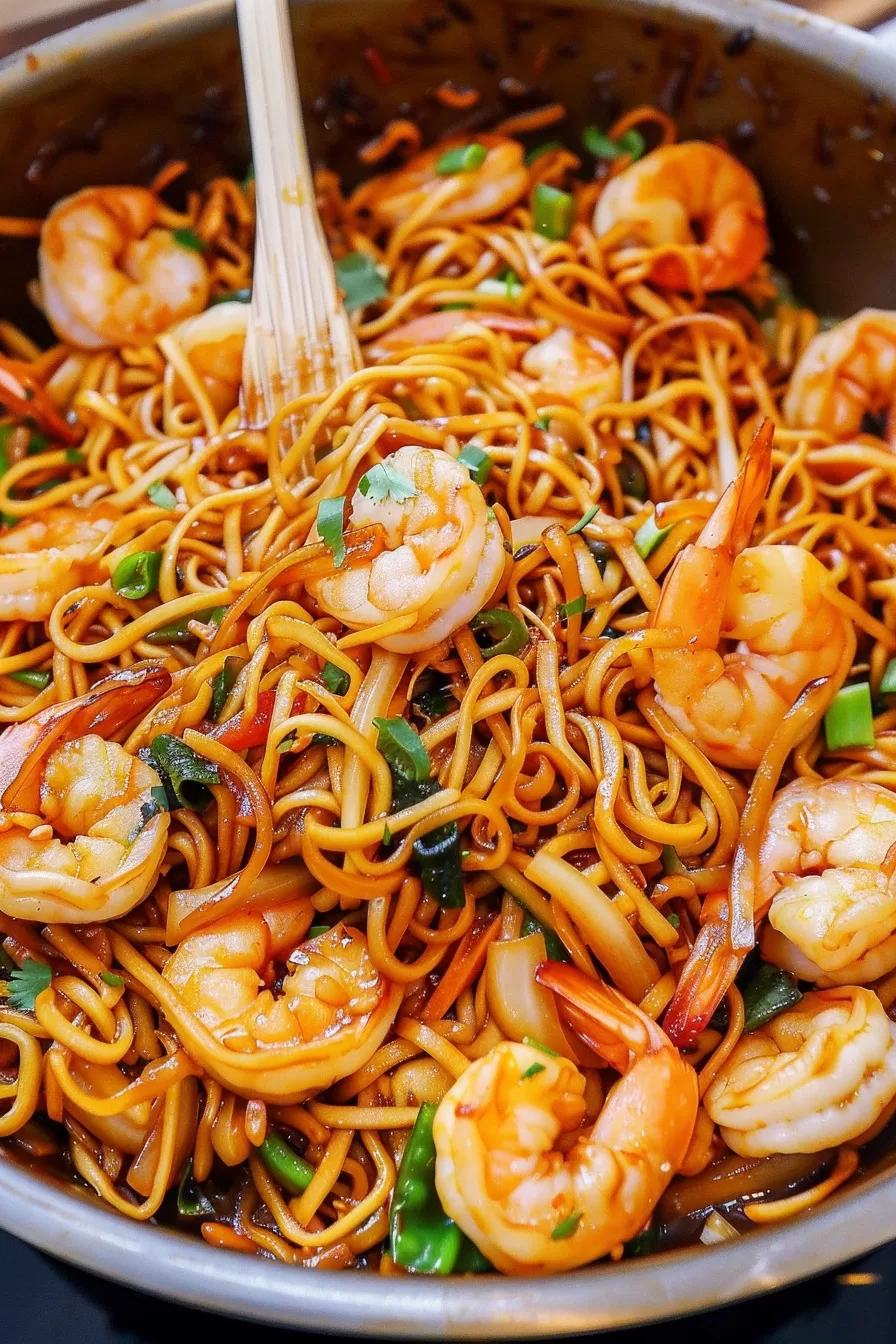 A bowl of shrimp lo mein noodles with tender shrimp, vegetables, and a glossy noodle coating, with chopsticks resting on the side.