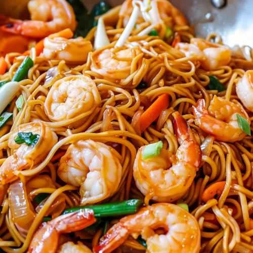 Close-up shot of shrimp lo mein noodles coated in a savory sauce with plump shrimp and fresh green onions, served in a skillet.