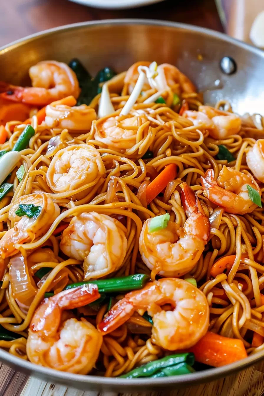 Close-up shot of shrimp lo mein noodles coated in a savory sauce with plump shrimp and fresh green onions, served in a skillet.