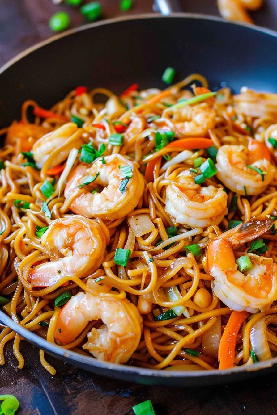 Stir-fried shrimp lo mein in a pan with colorful vegetables like carrots and green beans, featuring a glossy sauce and perfectly cooked shrimp.