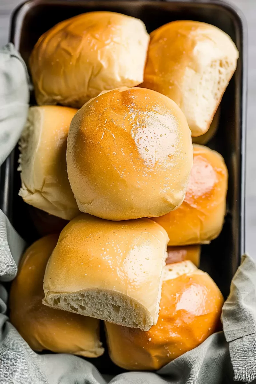 Close-up of soft, golden dinner rolls stacked in a pan, showing a fluffy interior.