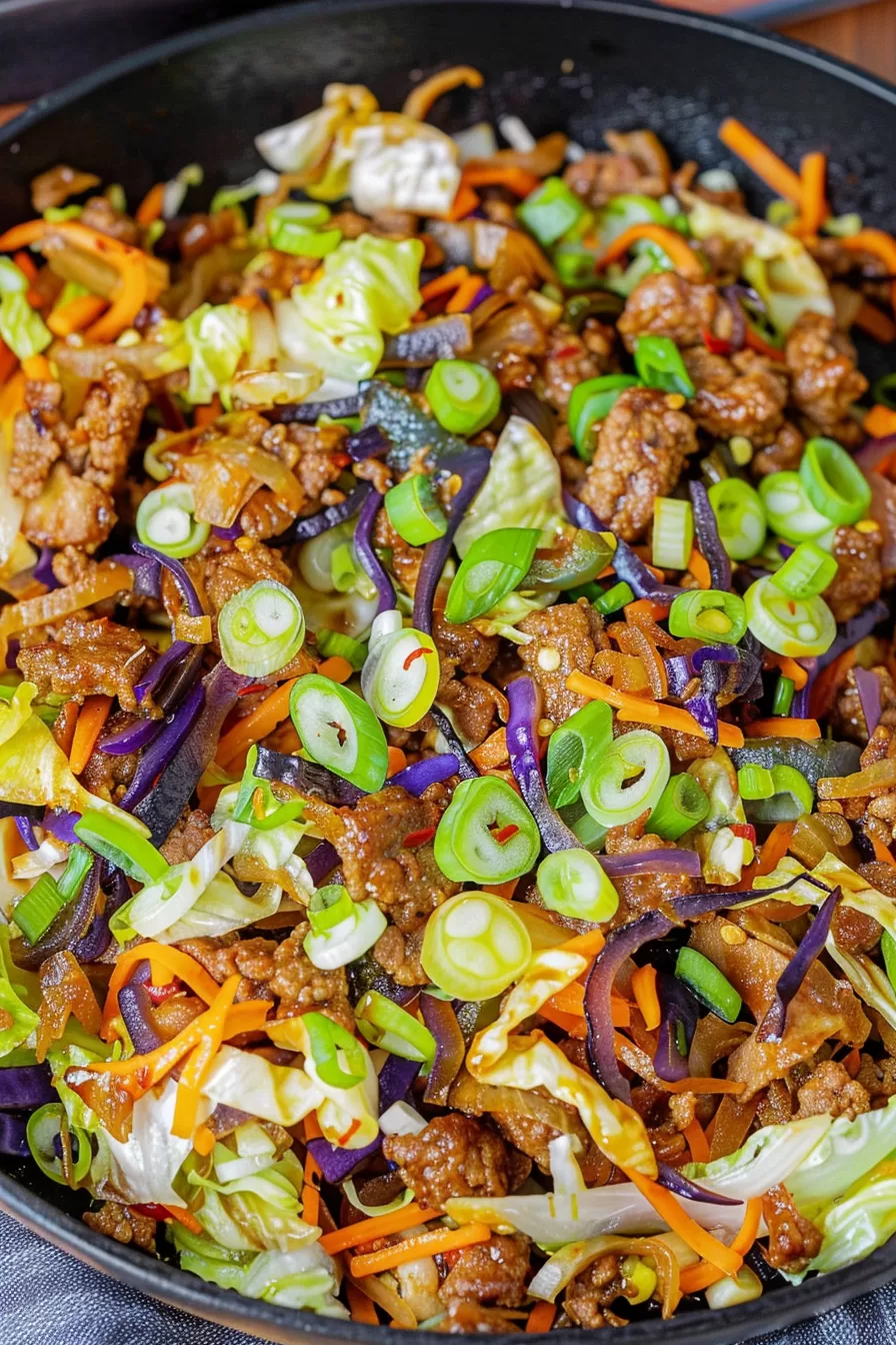 Close-up of stir-fried cabbage, carrots, and meat coated in a savory sauce, with purple cabbage adding a pop of color.