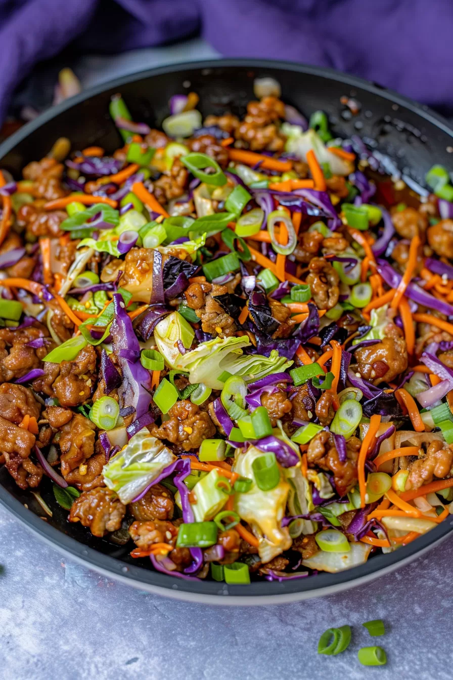 A skillet brimming with stir-fried cabbage, carrots, and onions, garnished with freshly chopped scallions.