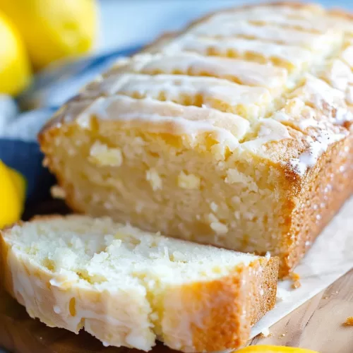 Side view of a lemon loaf slice with glaze dripping down, highlighting its moist interior.