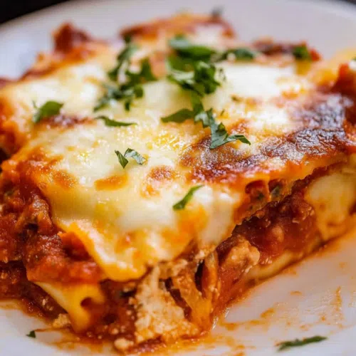 Side view of a whole lasagna in a baking dish, with golden-brown cheese bubbling on top.