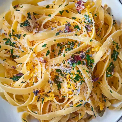 Close-up of perfectly cooked pasta with golden garlic slices and a sprinkle of red pepper flakes.