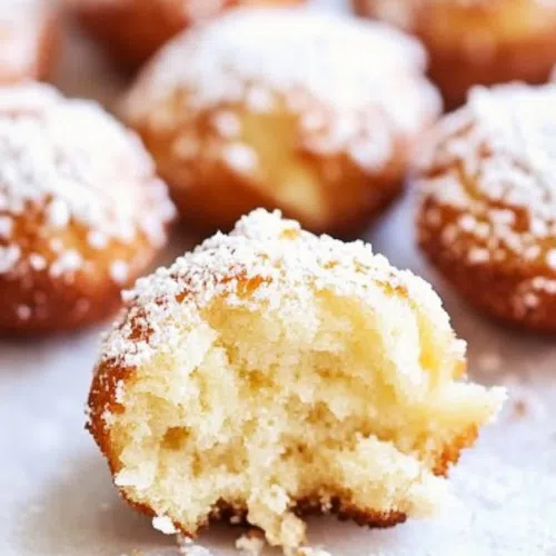 A single funnel cake bite with a bite taken out, showing the fluffy interior and crispy exterior.