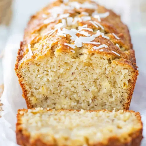 Close-up of a moist slice of banana bread featuring chunks of pineapple and a sprinkle of shredded coconut.