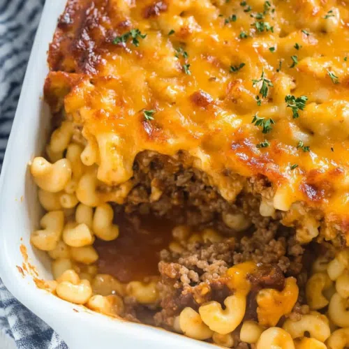 A delicious portion of meatloaf topped with gooey mac and cheese, garnished with fresh herbs.