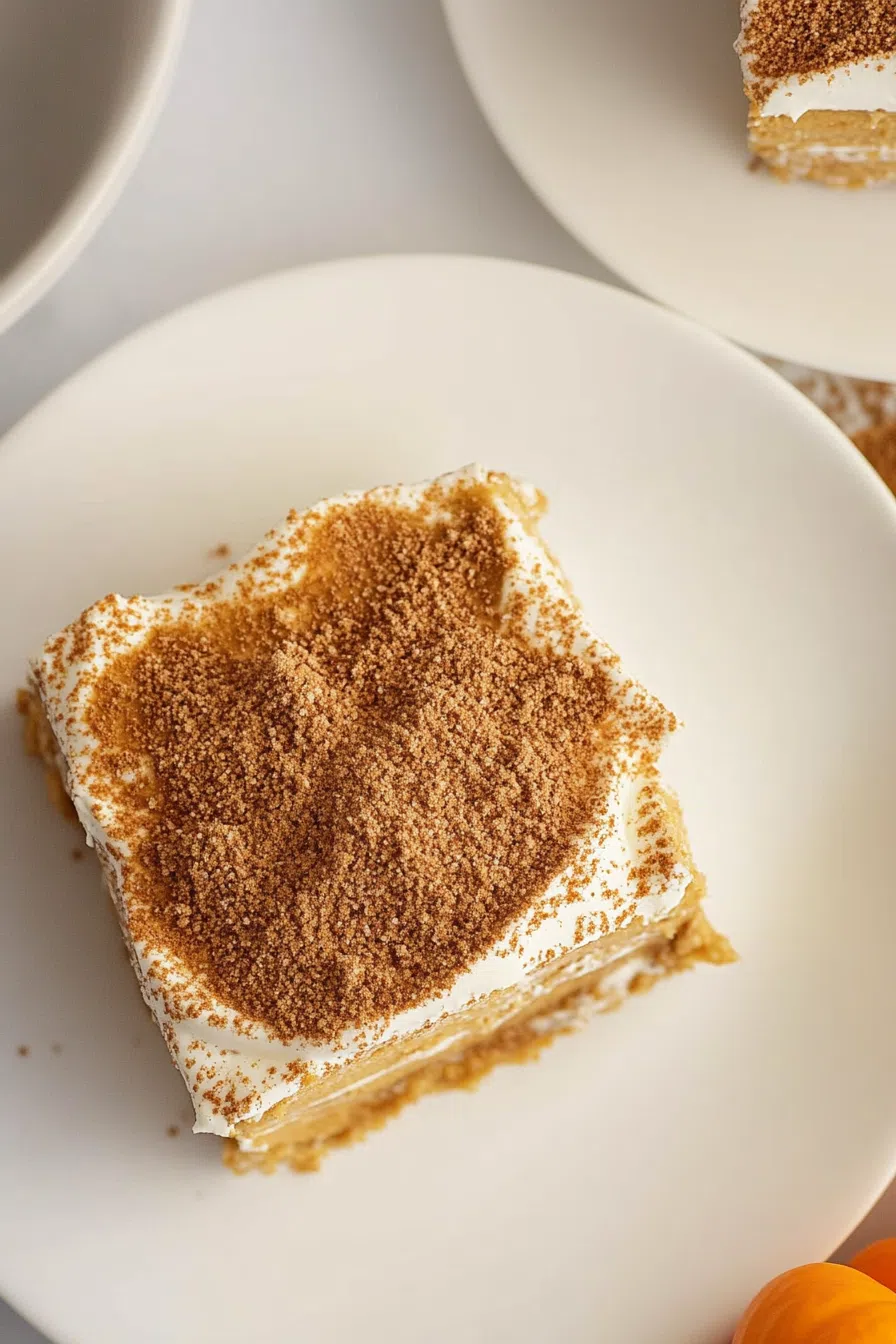 A creamy slice of no-bake pumpkin delight on a dessert plate, topped with whipped cream and a sprinkle of cinnamon.