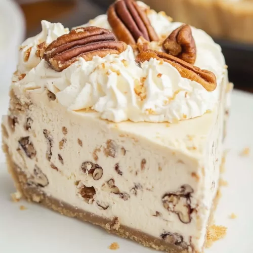 A creamy slice of pecan pie topped with whipped cream and crunchy pecans on a golden graham cracker crust.