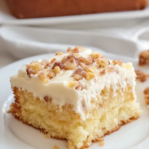 A freshly baked cake with thick frosting, topped with crushed pecans and pineapple, displayed in a baking dish.